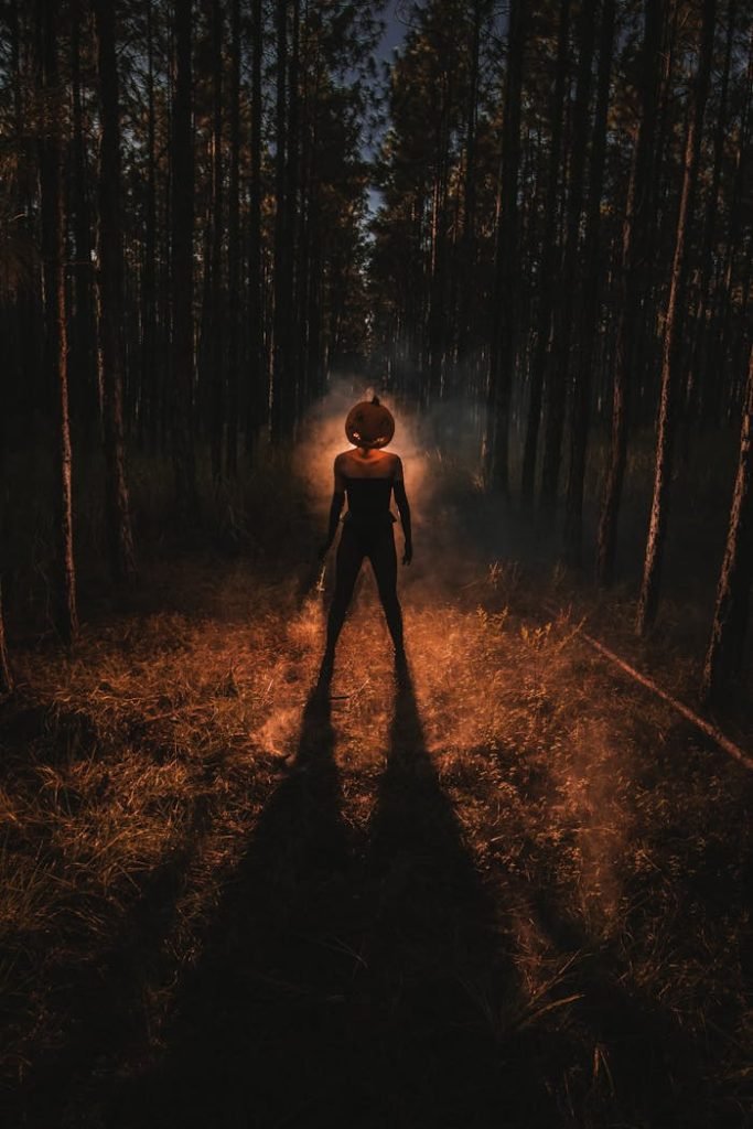 Eerie silhouette of person with pumpkin head in a misty, backlit forest. Perfect for Halloween themes.